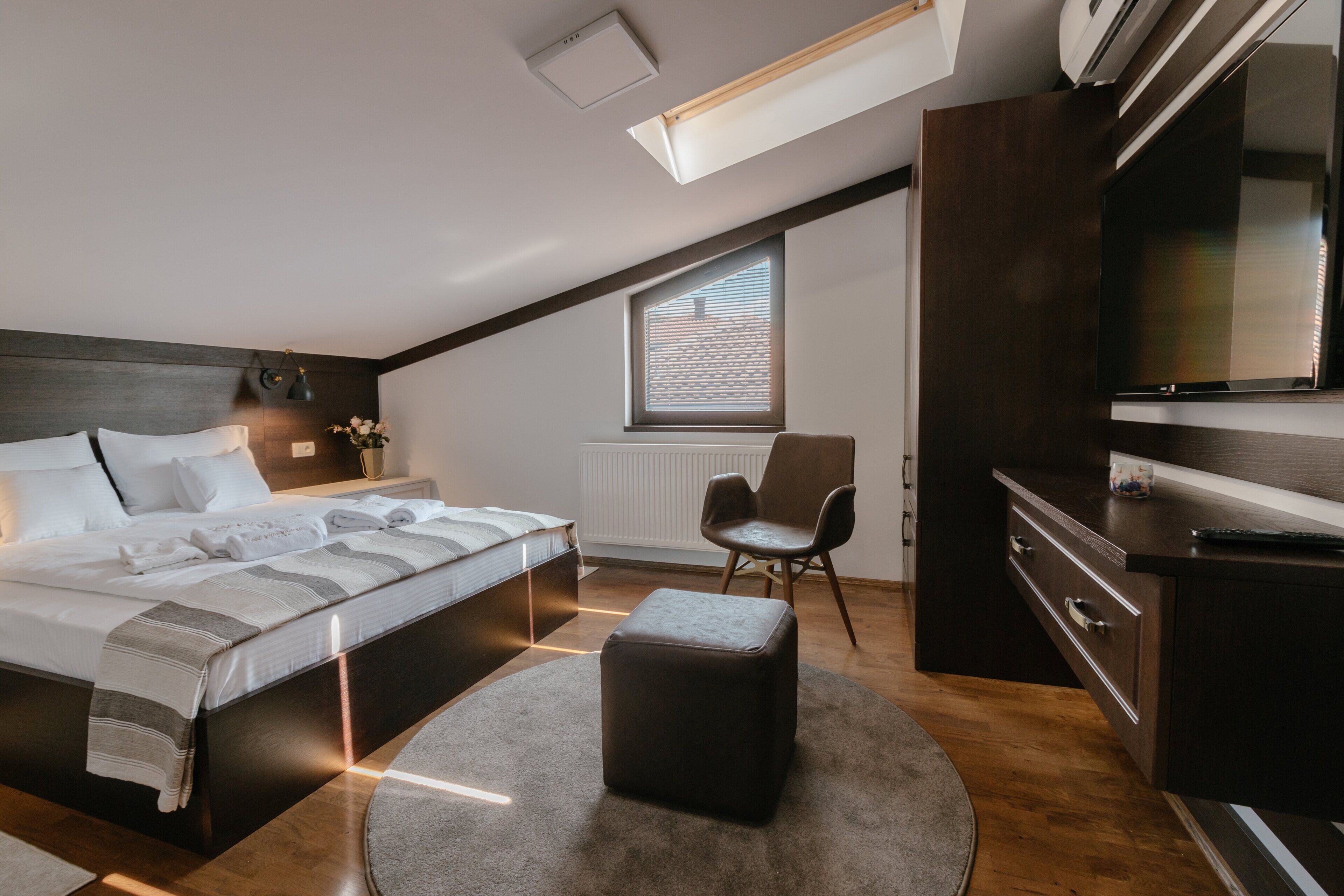 A modern bedroom with a large bed, a desk, a chair, and a television.