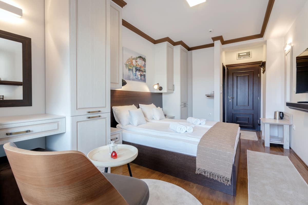 A modern hotel room with a large bed, a sitting area with a chair, a small table, and a desk.