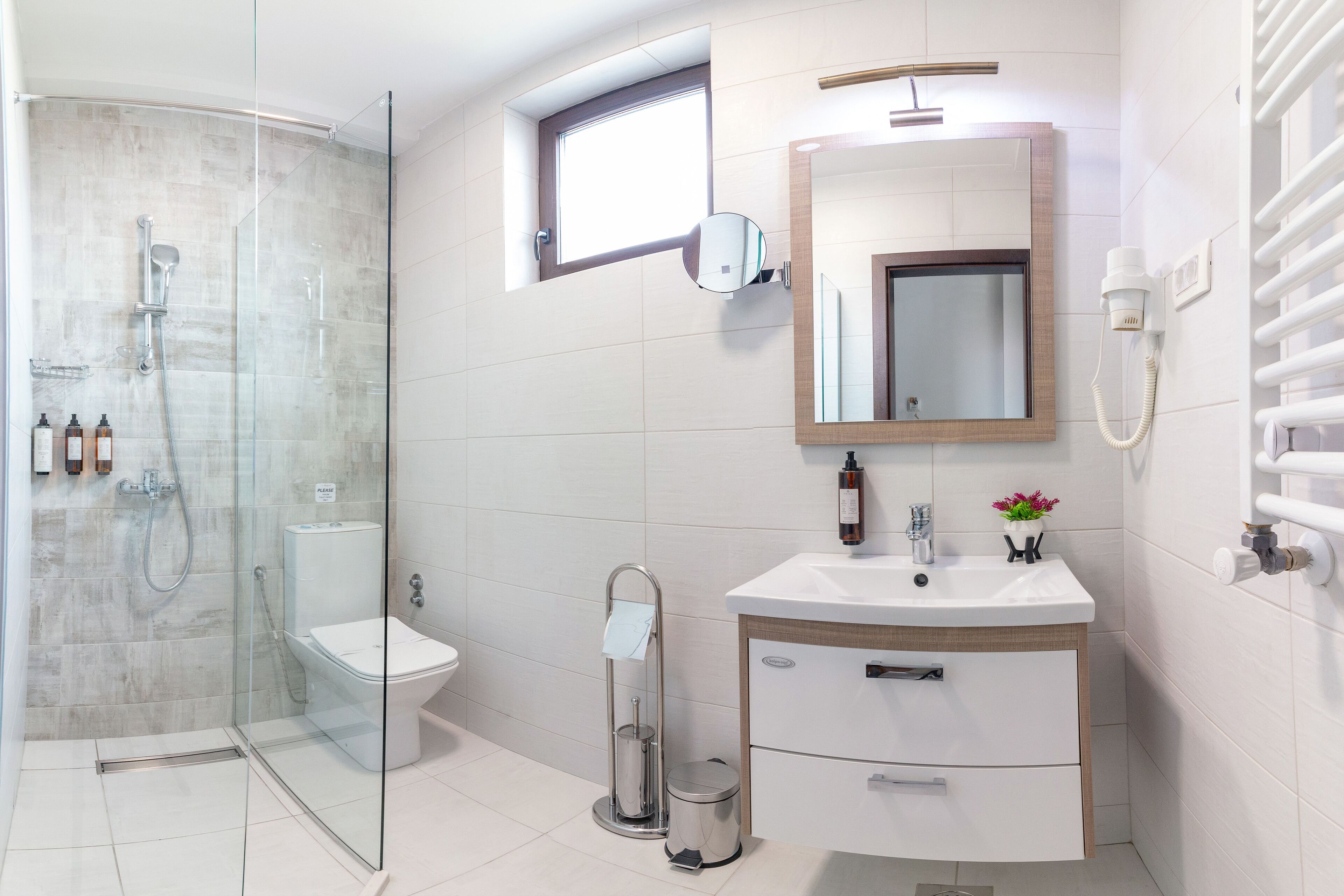 Un baño moderno con ducha envuelta en cristal, inodoro, lavamanos con espejo y un perchero para toallas.
