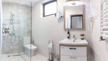 Un baño moderno con ducha envuelta en cristal, inodoro, lavamanos con espejo y un perchero para toallas.