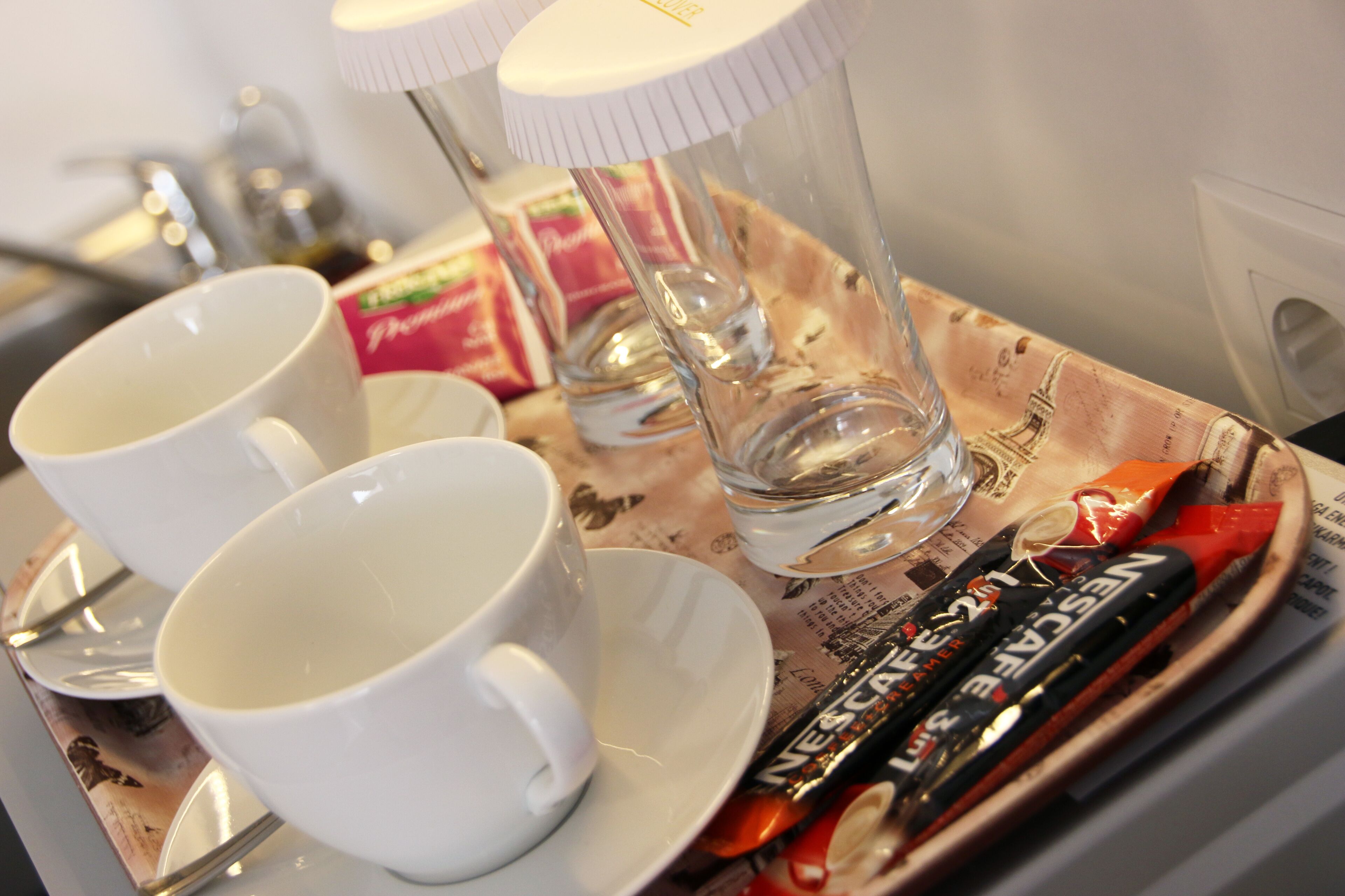 Una bandeja con dos tazas blancas, un vaso y un paquete de café instantáneo Nescafé.