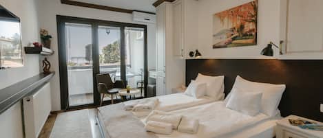 A hotel room with two beds, a large window, a balcony, and a painting on the wall.