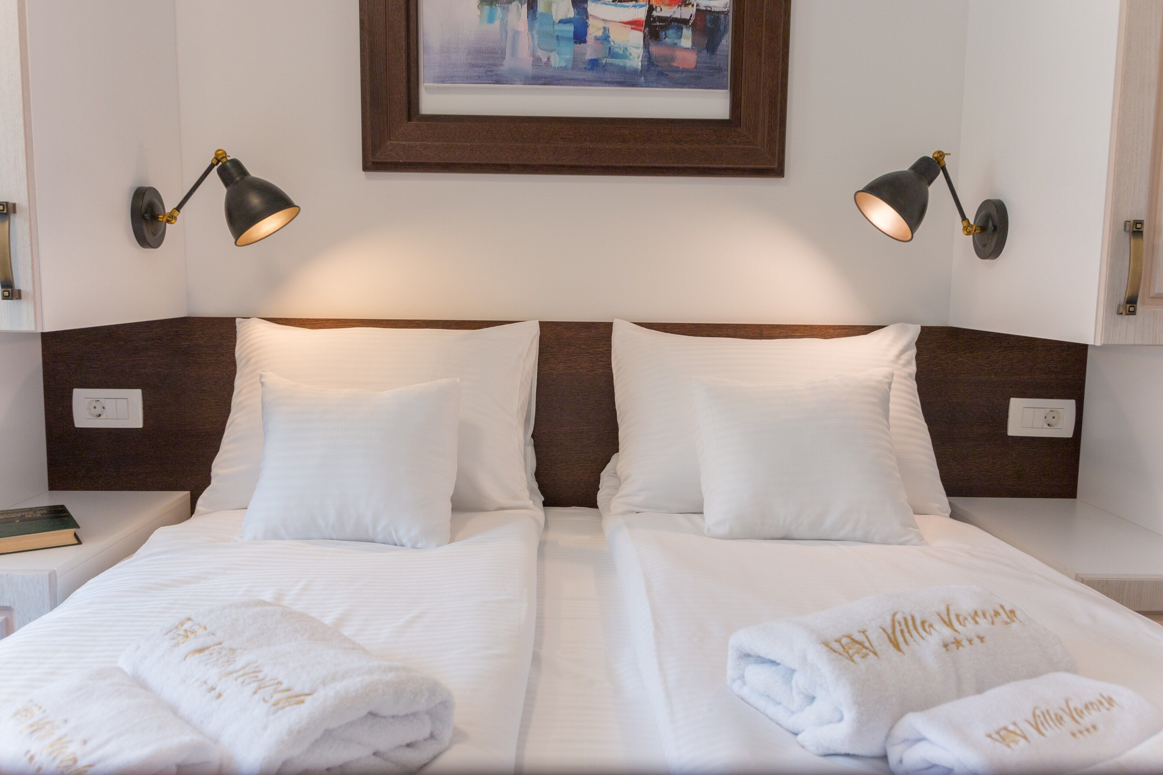Een tweepersoonsbed met witte lakens en twee bedlampjes.