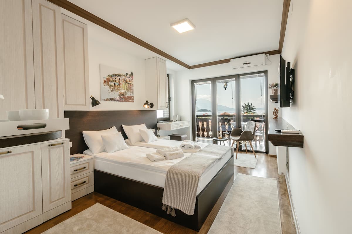 A modern bedroom with a large bed, bedside tables, a desk, and a balcony with a view.