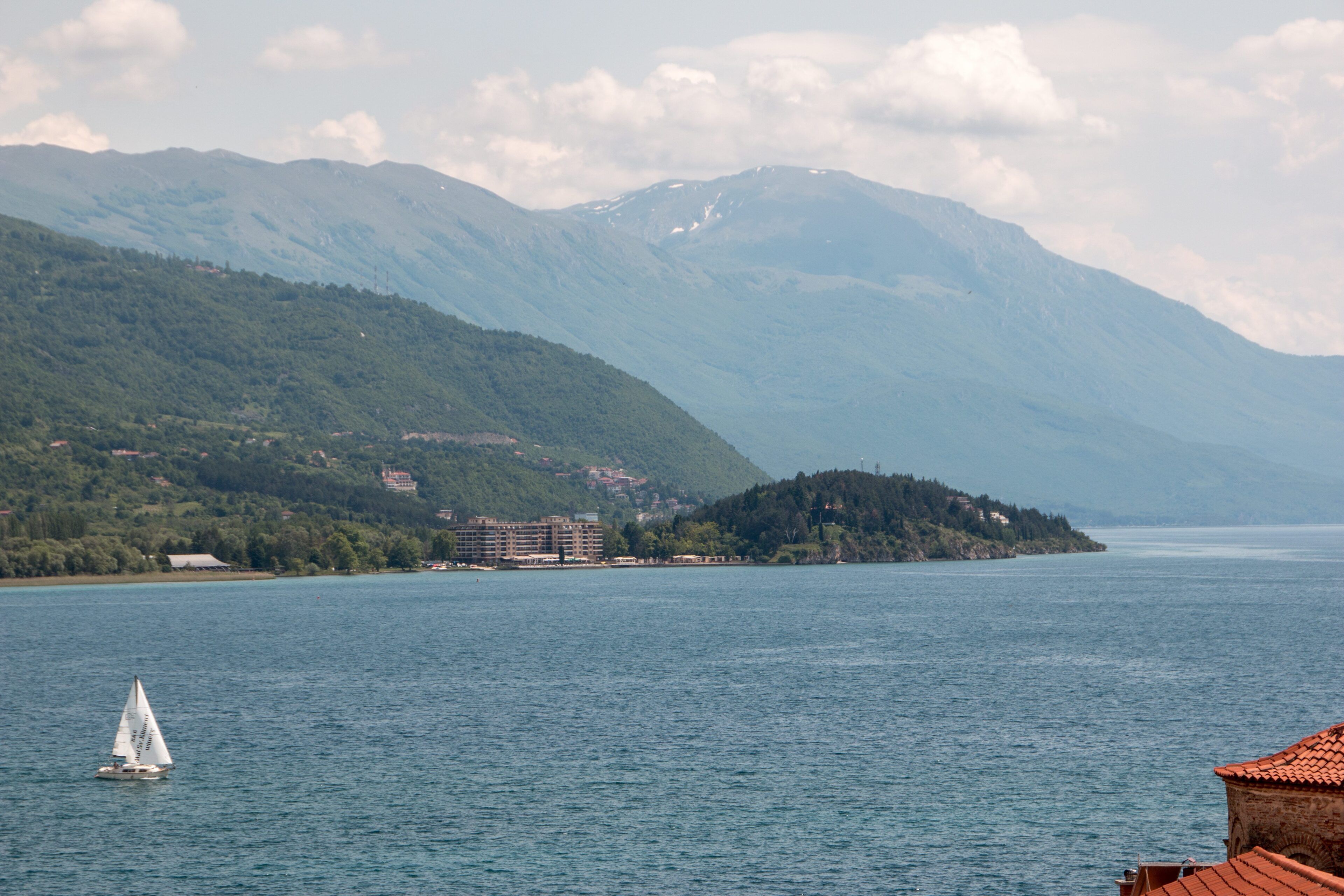 A lake with a sailboat, surrounded by mountains and buildings.