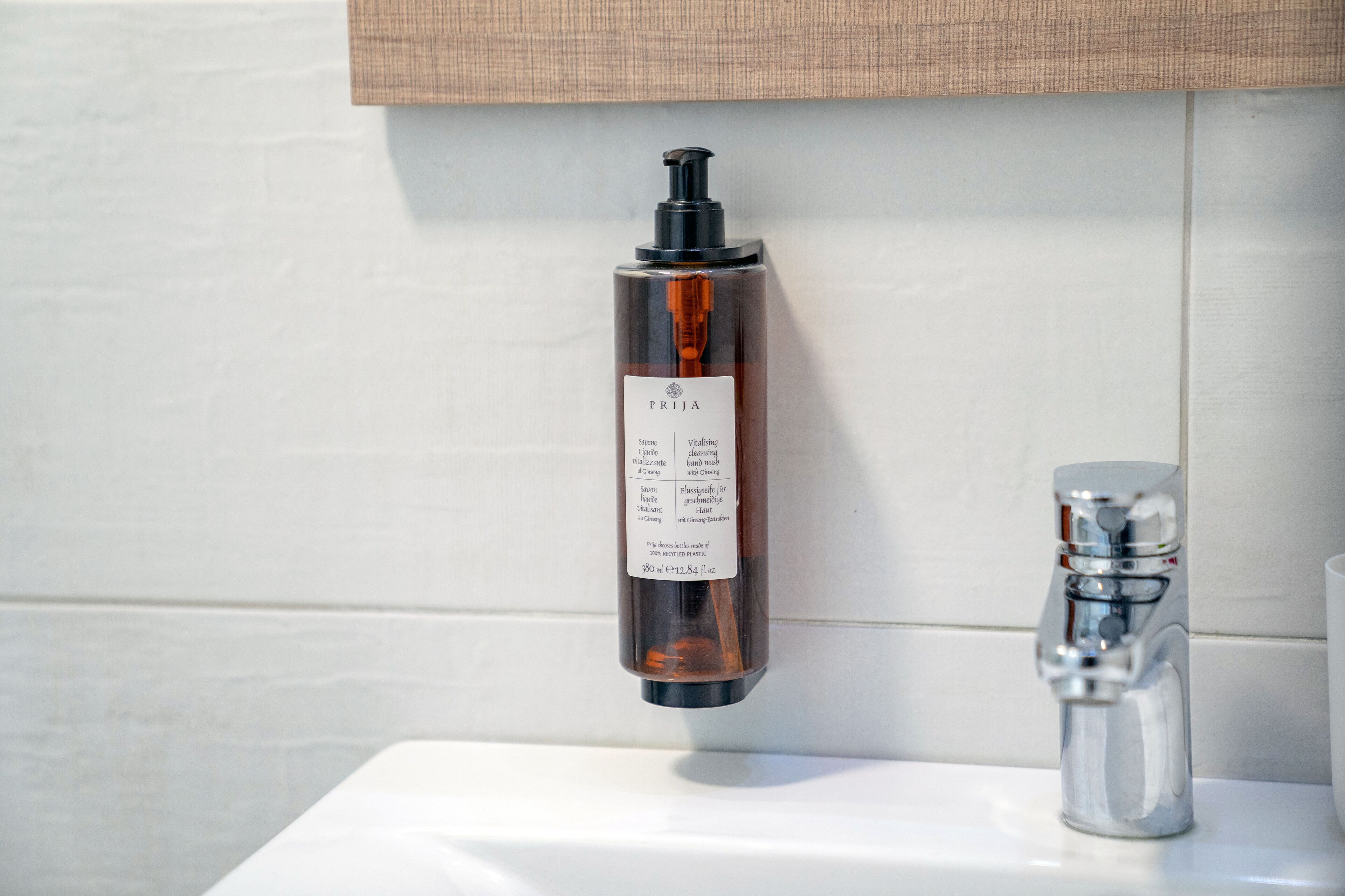 A bathroom with a white sink, a mirror, and a bottle of PRIJA soap.