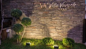 Un muro de piedra con el letrero "Villa Varosh" y tres macetas pequeñas con plantas.