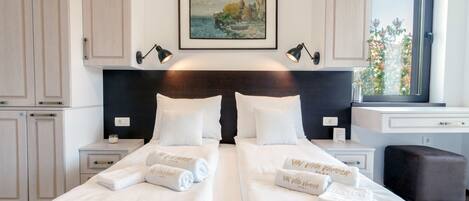 Una cama doble con ropa de cama y toallas blancas, un cuadro sobre la cama y una ventana con vistas a árboles.