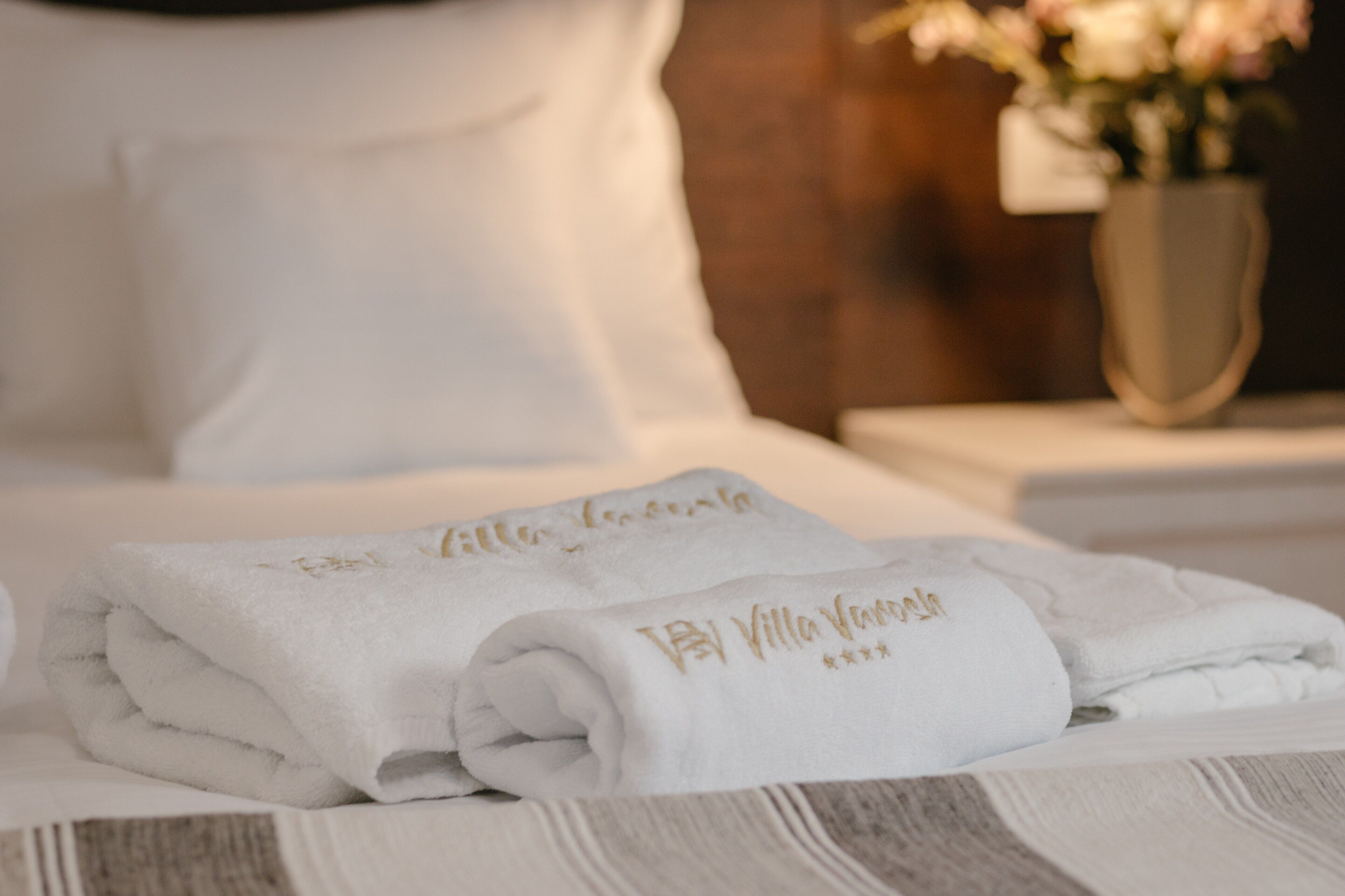 Una cama bien hecha con toallas blancas dobladas y un florero con flores en la mesita de noche.