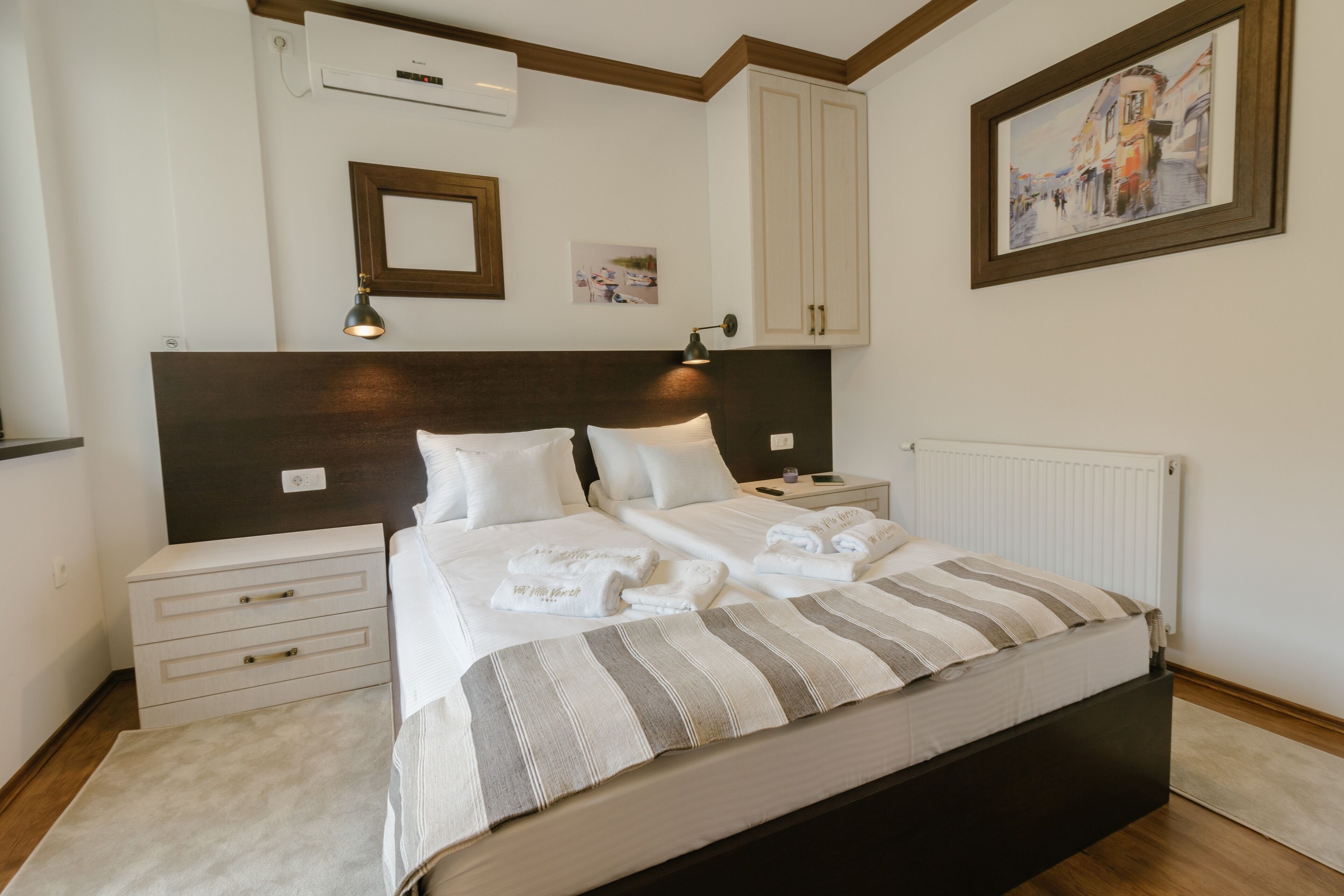 Una cama bien hecha con ropa blanca y ropa de cama a rayas, una mesita de noche con lámpara y un cuadro en la pared.
