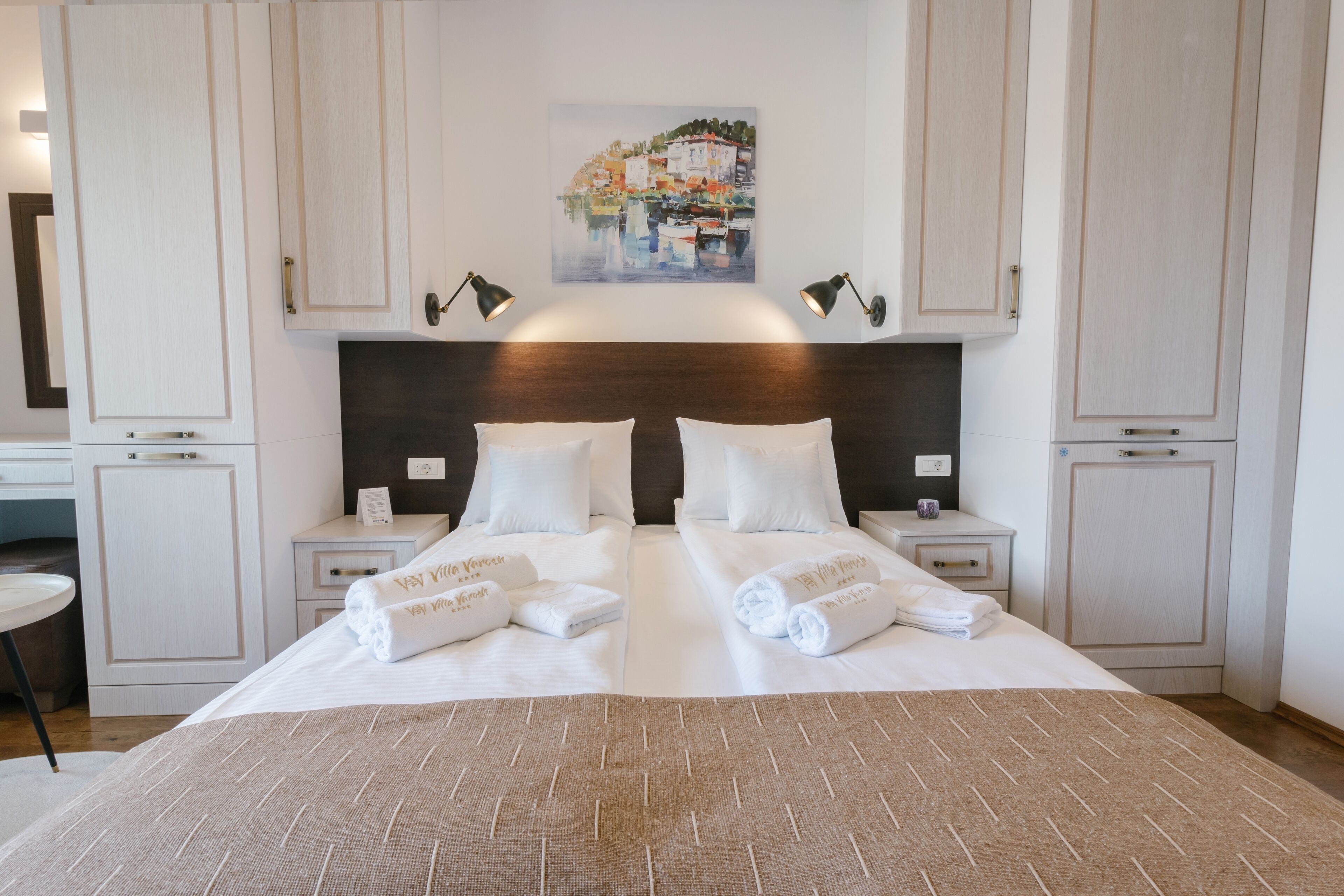 A hotel room with a large bed, two bedside tables, a headboard, and a painting above the bed.