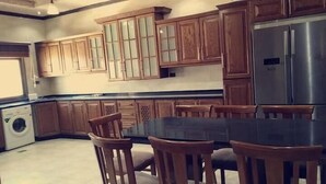 A kitchen with wooden cabinets, a stainless steel refrigerator, a washing machine, and a dining table with chairs. - Petra Villa (Wadi Musa)