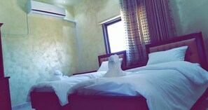 A bedroom with a bed, a window with curtains, an air conditioning unit, and a wall-mounted light fixture. - Petra Villa (Wadi Musa)