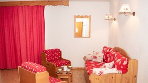 Una habitación acogedora con un sofá y un sillón de madera, una mesita con tazas y una cortina roja.