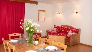 Un comedor con mesa de madera dispuesta para dos, un jarrón con flores y un sofá rojo con cojines estampados.