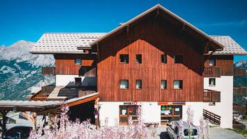 Un bâtiment en bois doté de nombreuses fenêtres et de balcons, un magasin de ski et un parking avec des voitures.