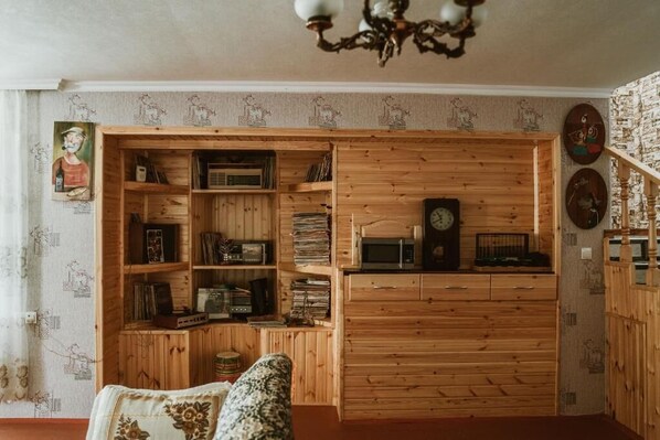 A room with a wooden bookshelf filled with books and records, a vintage radio, and a clock.