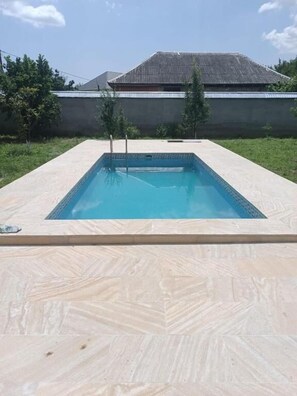 A rectangular swimming pool with a tiled edge, surrounded by a light-colored tiled deck.