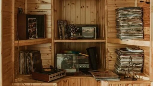 Una estantería de madera con varios objetos, entre ellos libros, CDs y adornos.