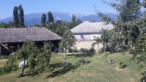 Un edificio rústico con techo de lámina corrugada, rodeado de un área con césped, árboles y una vista despejada de montañas lejanas.