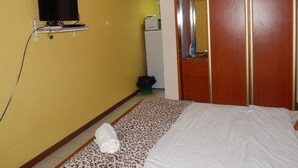 Une chambre comprenant un lit, un téléviseur fixé au mur, un four à micro-ondes et une armoire.