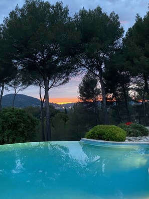 A swimming pool surrounded by trees and a view of a sunset over a hilly landscape. - Une Pause en Provence (Le Beausset)
