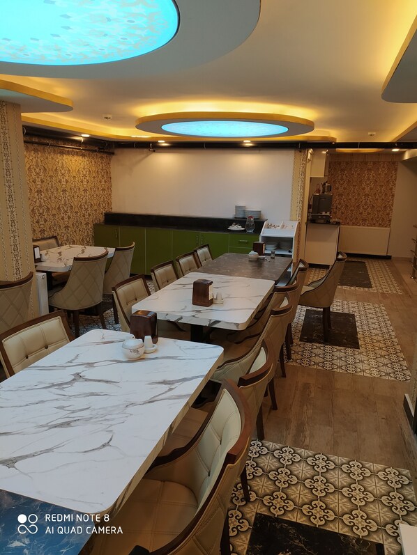 A restaurant with marble-topped tables and cushioned chairs, a green counter, and patterned walls. - Akdeniz Van Otel (Van)