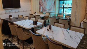A restaurant with marble-topped tables and cushioned chairs, a flat-screen TV, and patterned wallpaper. - Akdeniz Van Otel (Van)