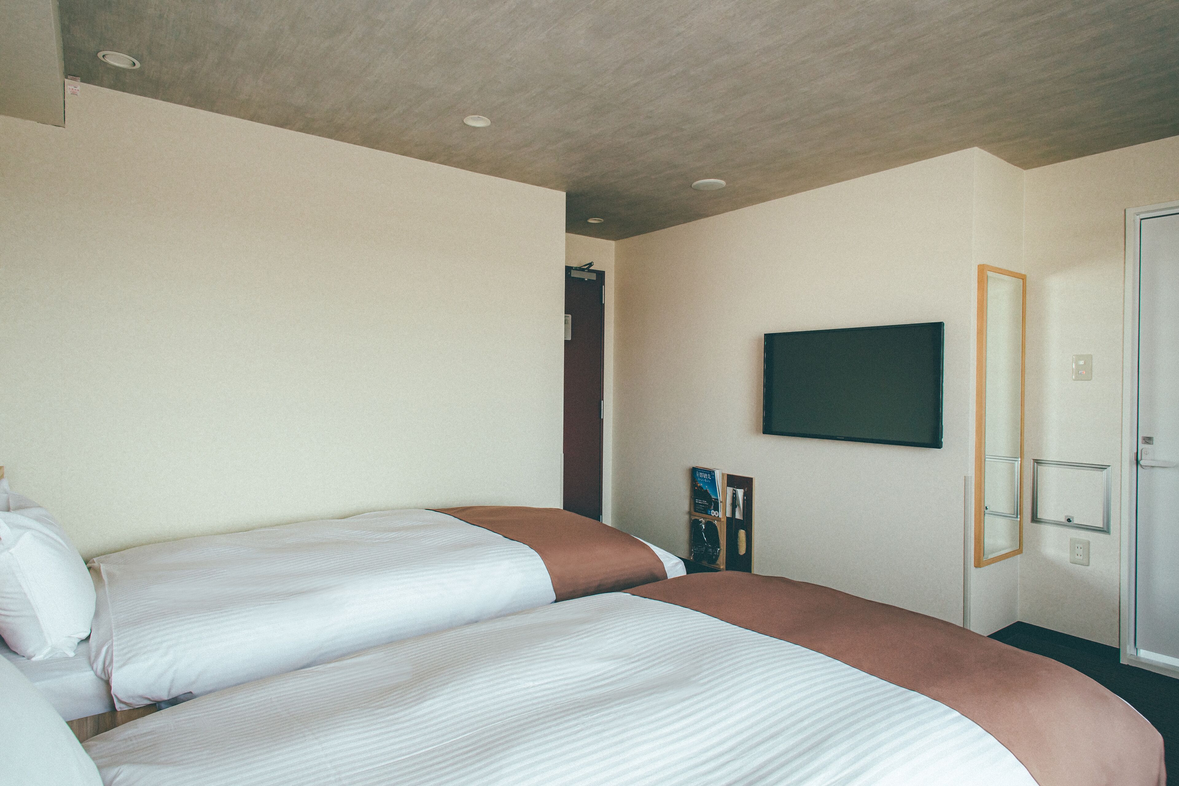Une chambre d’hôtel avec deux lits, un téléviseur à écran plat fixé au mur et une porte donnant accès à une salle de bain.