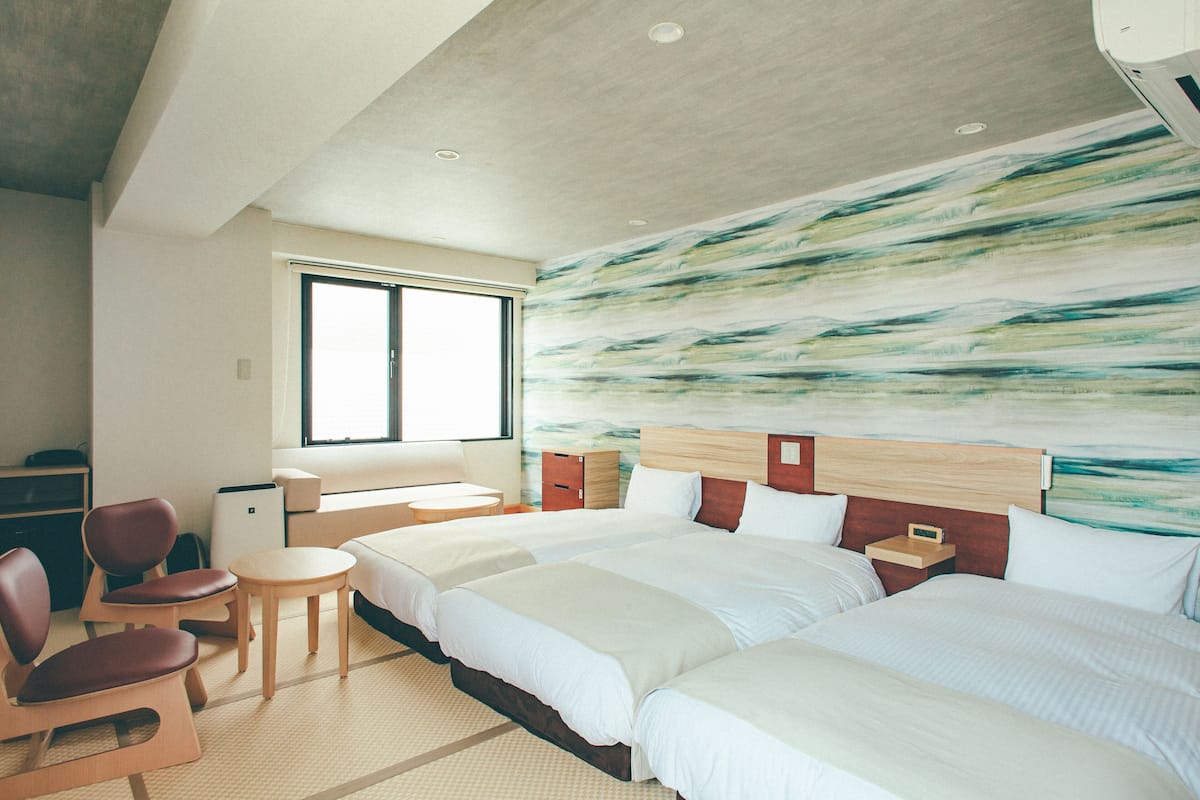Une chambre d’hôtel avec deux lits, une petite table, une chaise et un grand tableau abstrait accroché au mur.