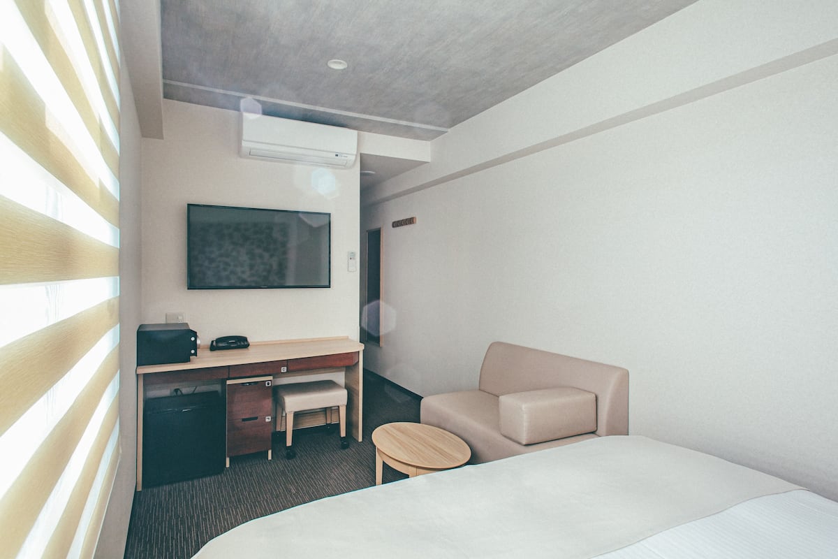 Une chambre d’hôtel comprenant un lit, un bureau avec une chaise, une petite table ronde, un canapé et un téléviseur à écran plat fixé au mur.