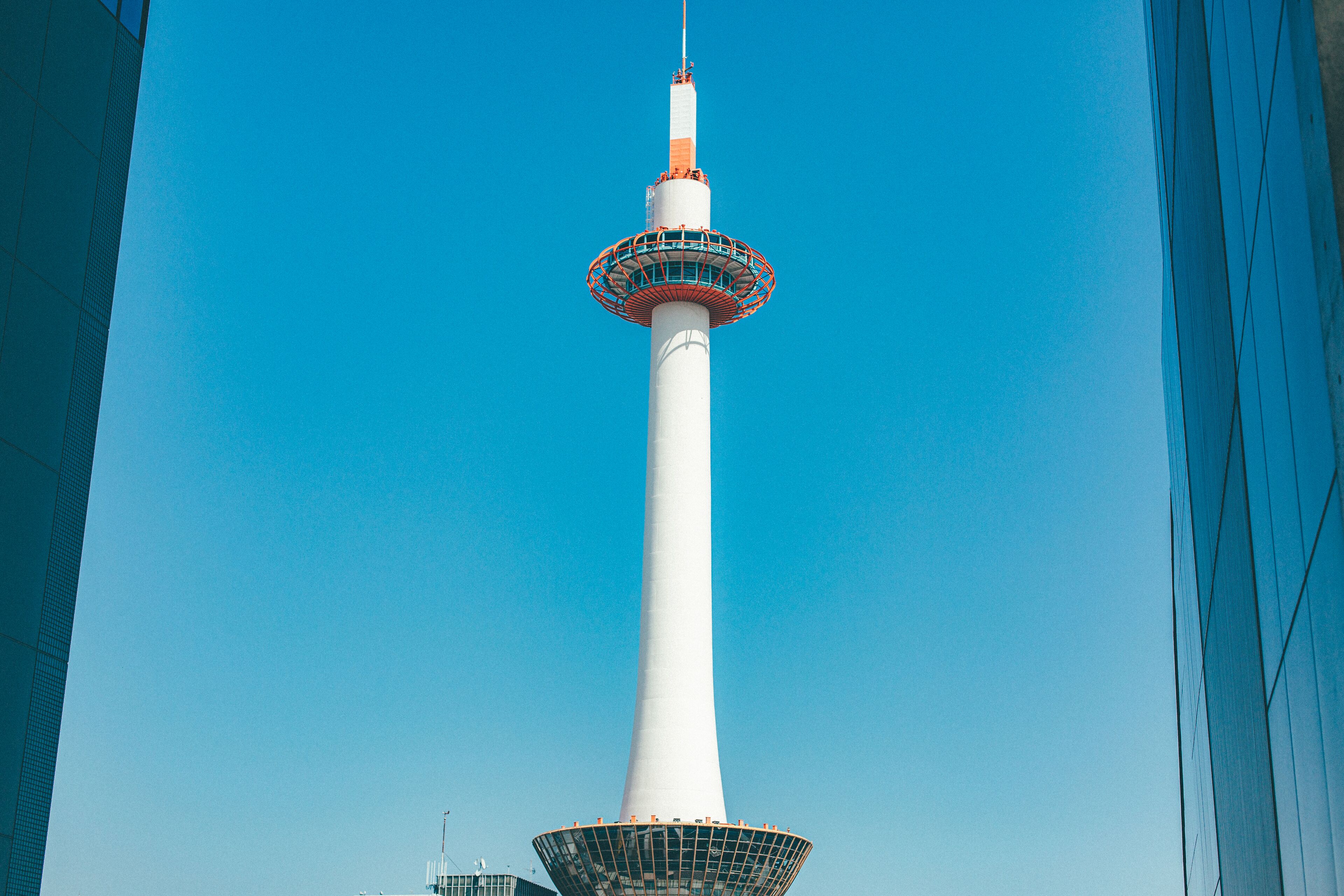 Een hoge witte toren met een rond uitkijkplatform bovenop, tegen een helderblauwe lucht.