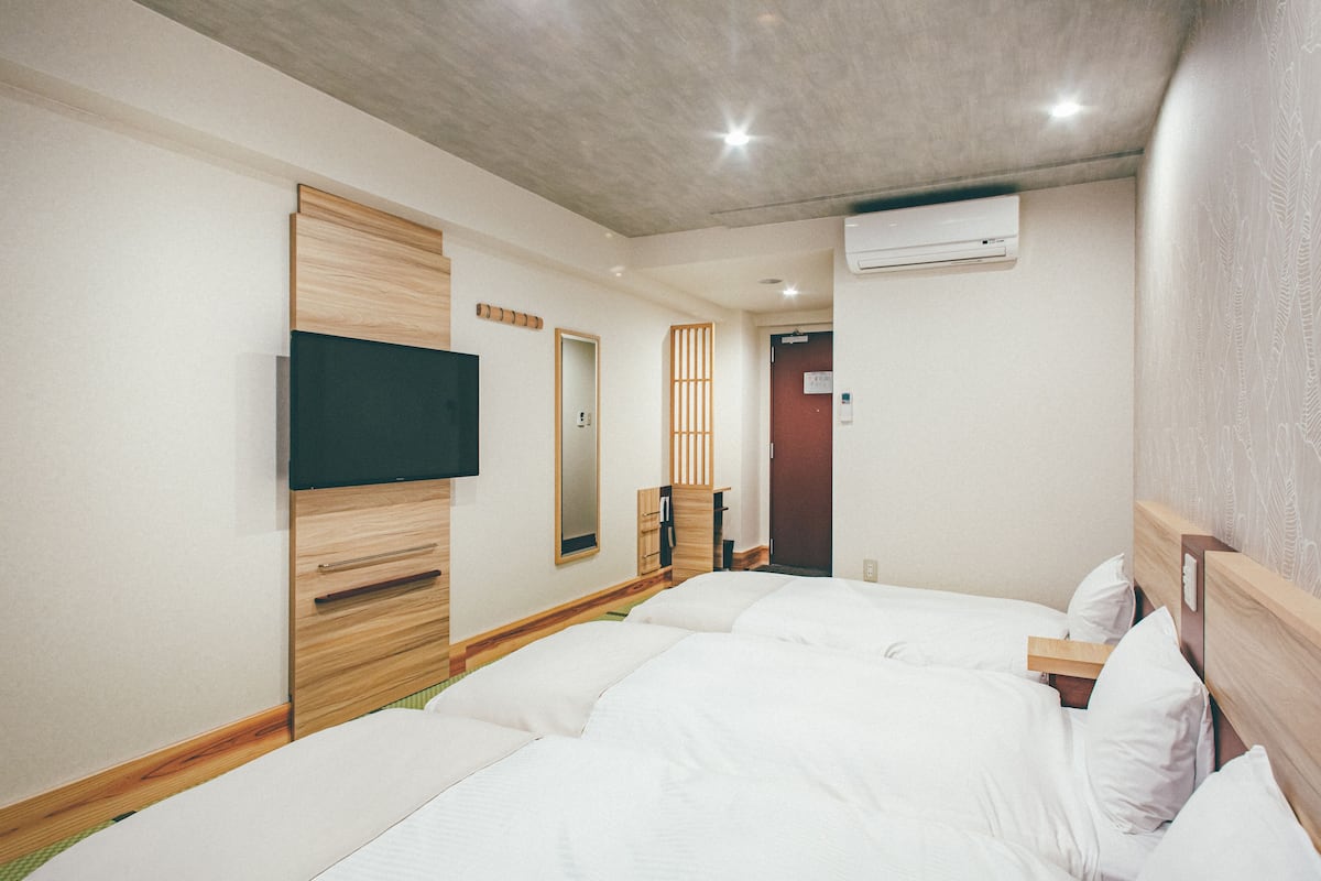 Une chambre d’hôtel avec deux lits, une tête de lit en bois, un téléviseur à écran plat et un appareil de climatisation.