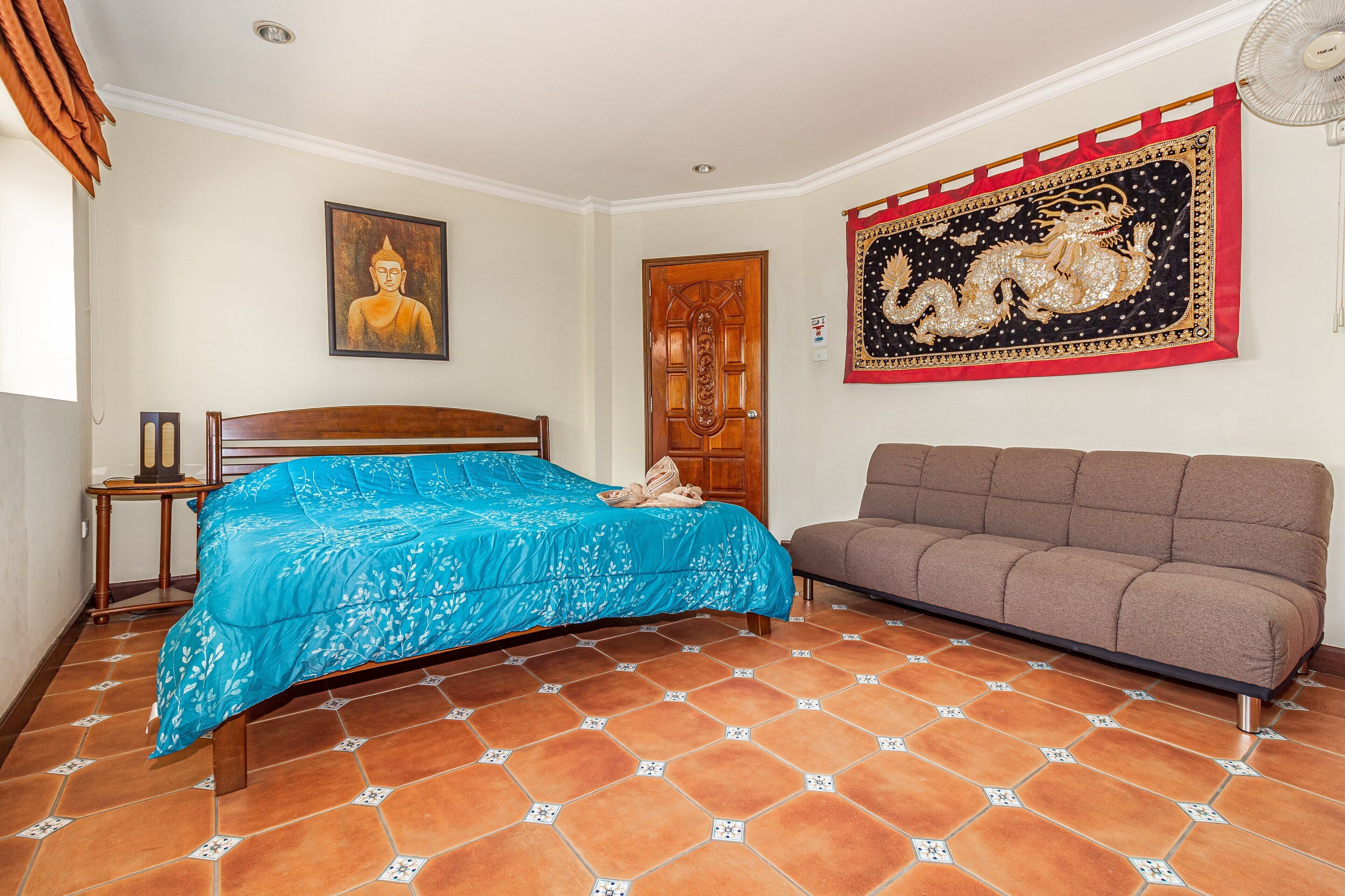 A bedroom with a bed, a sofa, a wooden door, and a wall with a tapestry.