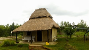A thatched-roof hut with a bench outside, surrounded by greenery. - Backpackers Eco Village (Gosaba)