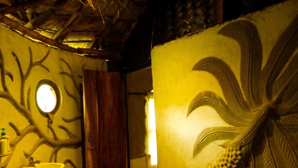 A bathroom with a wooden door, a sink, and a wall with a tree branch design. - Backpackers Eco Village (Gosaba)