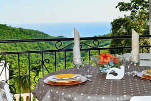 Ein Esstisch mit Blick auf eine üppige grüne Landschaft und das Meer im Hintergrund.