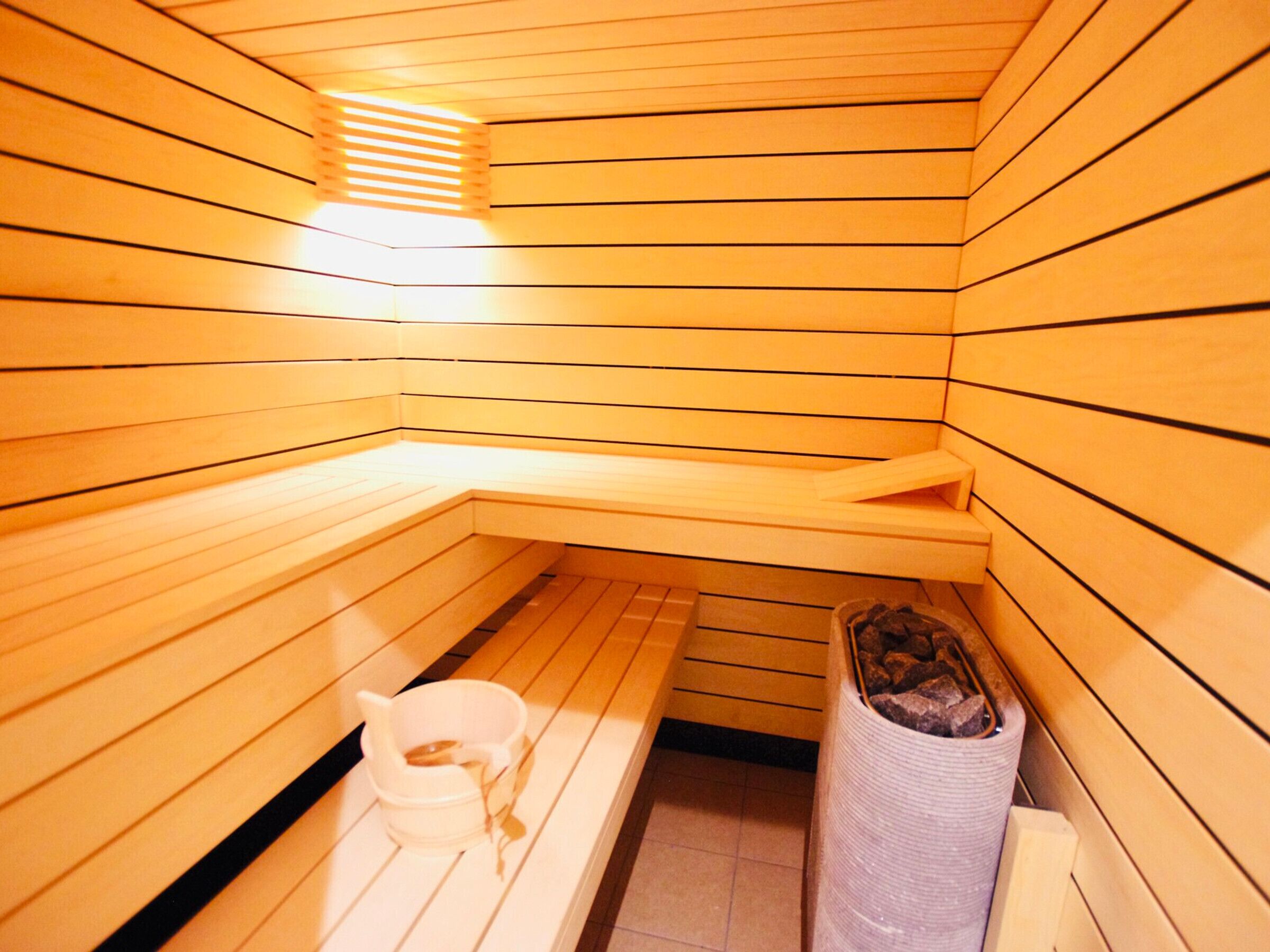 A sauna with wooden walls and benches, a small trash bin, and a towel rack.