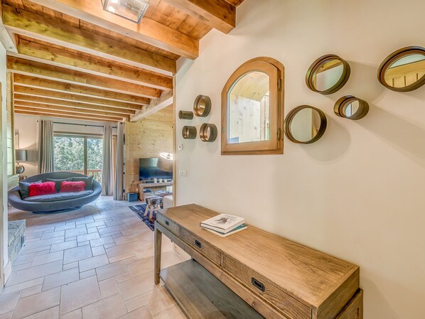 A modern interior with a wooden ceiling, a cozy seating area with a round chair, a wooden console table, and a large mirror on the wall.