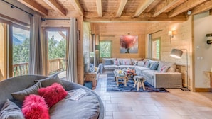 Un salon spacieux avec un grand canapé, une table basse et une cheminée. Il y a un balcon avec vue sur les montagnes.