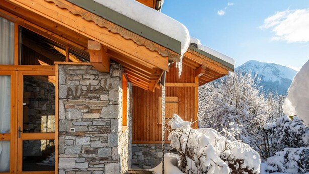 Un chalet en bois aux murs de pierre, doté d’un porche en bois et surplombant un paysage montagneux.