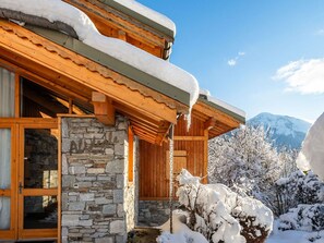 A wooden chalet with stone walls, a wooden porch, and a mountain backdrop.