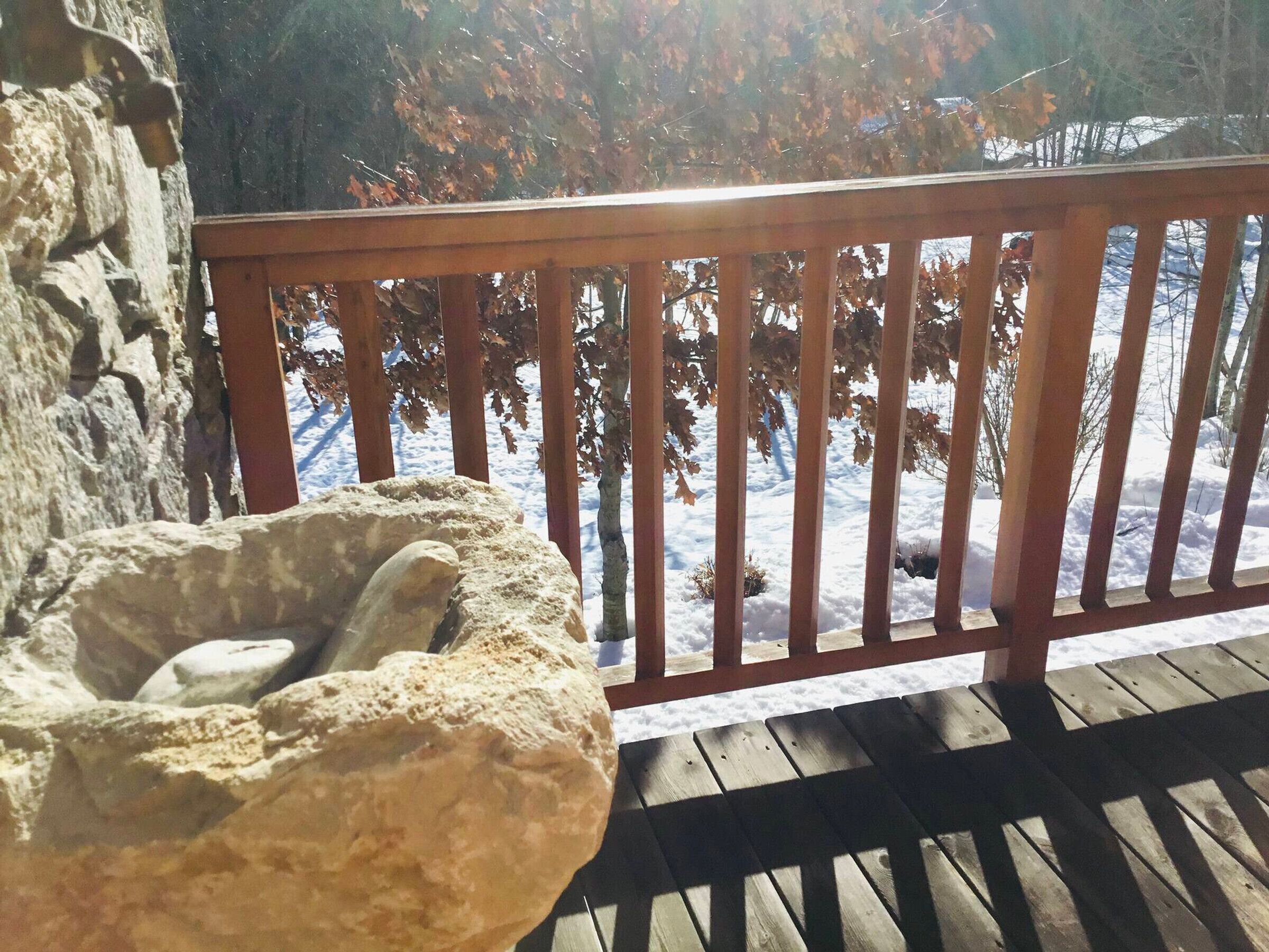 A wooden deck with a stone feature and a view of a snowy landscape with trees.