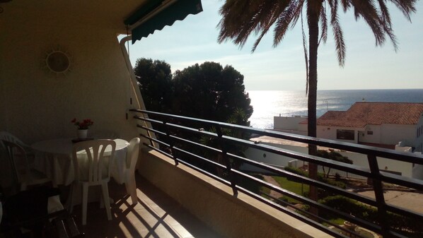 Un balcón con mesa y sillas, con vistas a la costa, palmeras y edificios.