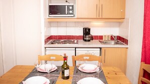 Cocina pequeña con microondas, cafetera y lavamanos. Se observa una mesa de comedor con platos y una botella de vino.