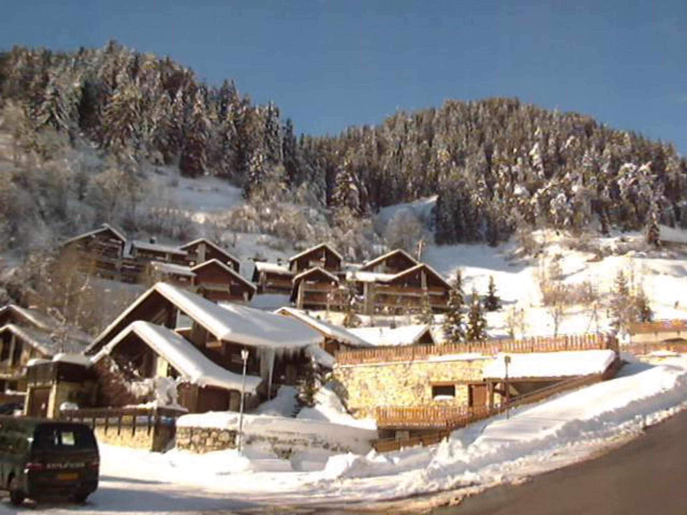 A row of wooden cabins with snow-covered roofs, set against a backdrop of a snow-covered mountain.