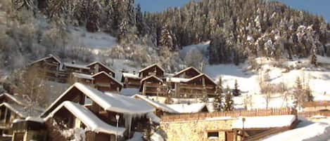 A row of wooden cabins with snow-covered roofs, set against a backdrop of a snow-covered mountain.