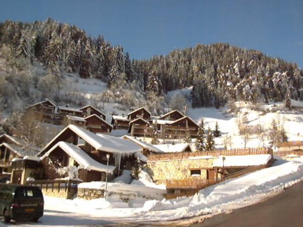 A row of wooden cabins with snow-covered roofs, set against a backdrop of a snow-covered mountain.