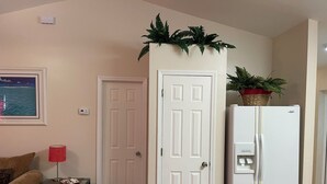 A room with a beige wall, a white door, a white refrigerator, a small table with a red lamp, and a framed picture. - TAMPA FLORIDA VACATION DELIGHT (Tampa)