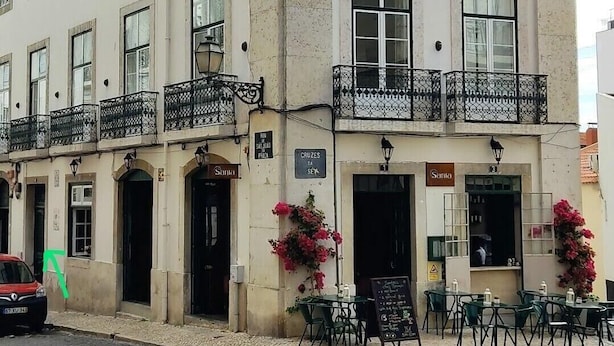 A two-story building with a ground-floor cafe named 'Santo' and a visible sign for 'Cruzes SEK'. - No Limit Alfama Guesthouse (Lisbon)